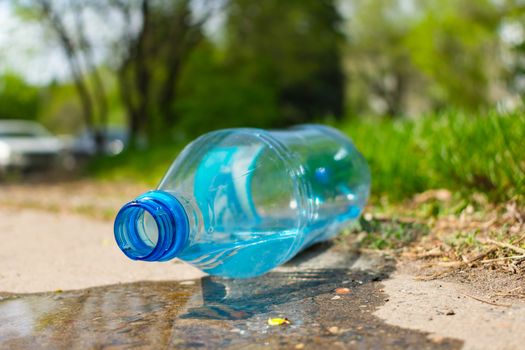 Environmental pollution by plastic bottles. A plastic bottle lies on the pavement in a park