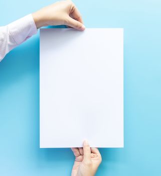 close up of two hands holding  empty white blank letter paper size A4 with copy space for flyer or invitation mock up isolated on a blue background.