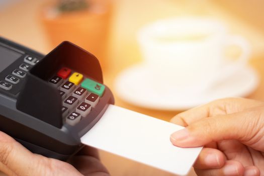 credit card payment concept. close-up hand insert credit card mock up with white blank card with a card swipe machine at point of sale terminal in coffee shop