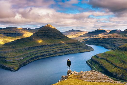 Hiker enjoys spectacular views over fjords from the summit of a mountain near Funningur on Faroe Islands.