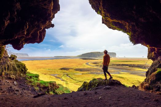 Hiker in the Loftsalahellir Cave near the village of Vik overlooking the beautiful landscape of Iceland with a road passing by.