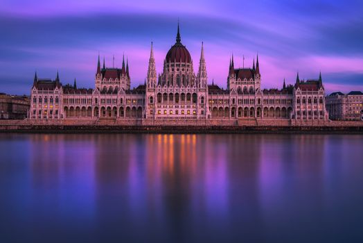 Hungarian Parliament Building built in the Gothic Revival style in Budapest viewed at sunset with Danube river in the foreground. Long exposure.