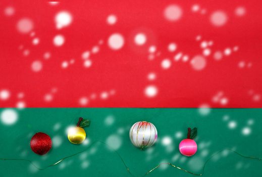 Baubles and fruits with golden string on green and red background for christmas with copy space with snow fall
