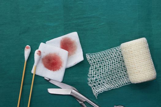 Gauze,blood,scissors,roll gauze and two swab cotton bus sticks on green medical surgical dress and copy space
