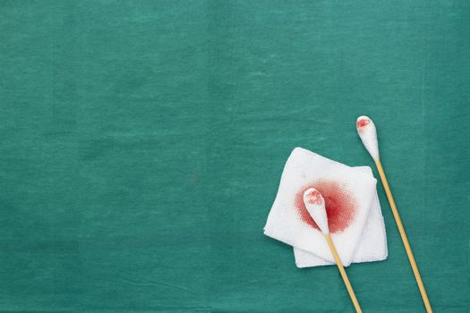 Gauze,blood and two swab cotton bus sticks on green medical surgical dress with copy space