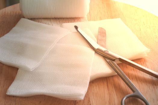 Gauzes, scissors and roll gauze on wooden table with sun flare