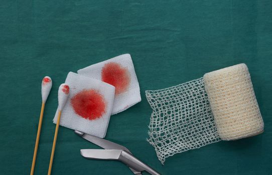 medical tools include scissors, swabs,net roll gauze and blood gauze on green surgical dress  for clean wound
