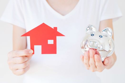 Hands holding a piggy bank and a house model.