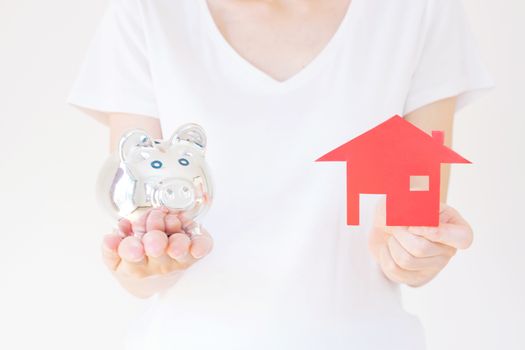 Hands holding a piggy bank and a house model.