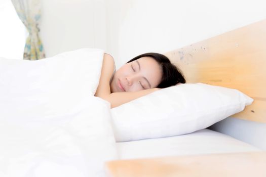 A woman resting in bed with hands beside her head on the pillow.