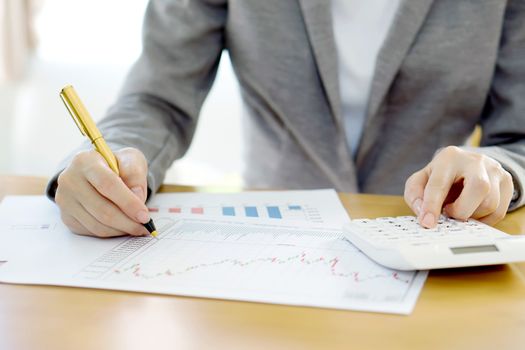 Close-up Of Businesswoman Analyzing Financial Report With Calculator At Wooden 