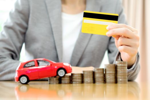 Businesswoman hand hold credit card, a toy car and a stack of coins