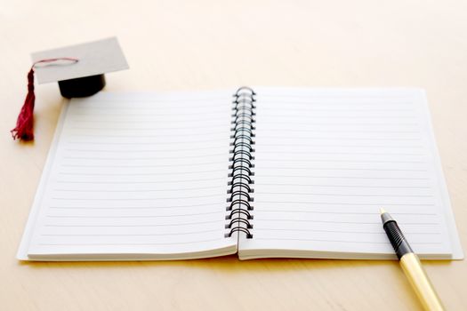 Blank notebook on the table and graduation cap