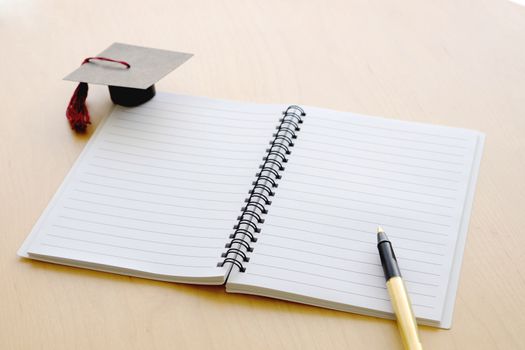 Blank notebook on the table and graduation cap