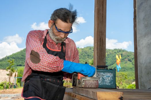 Senior man carpenter at work using Jointer Plane,bearded craftsman with grey hair is good at working with planks.