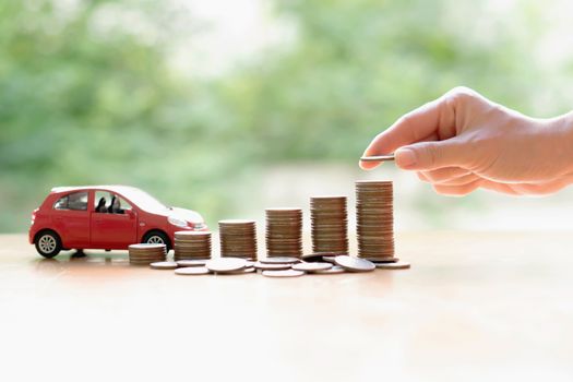 Businesswoman hand pushing a toy car over a stack of coins