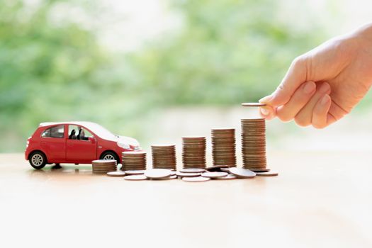 Businesswoman hand pushing a toy car over a stack of coins