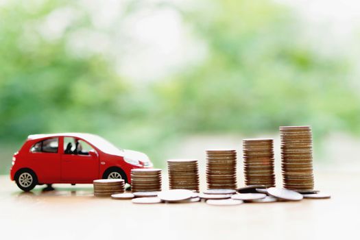 Stacks of giant silver coins next to a new red car 