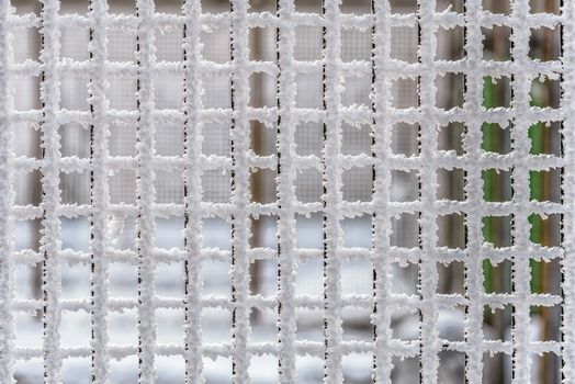 Squared cells of a metallic wire fence completely covered with frost during a cold winter with subzero temperatures