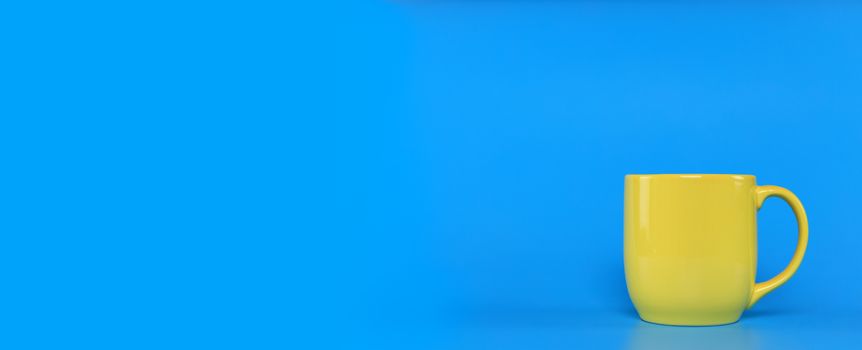 Yellow cup with handle on blue background with copy space