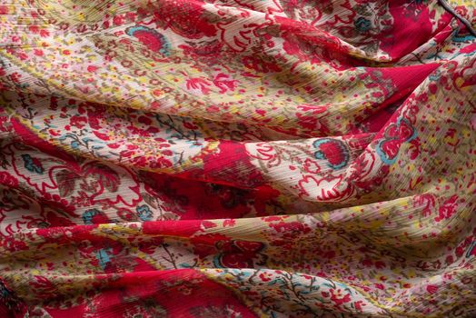 Soft folds of a multicolored synthetic fabric texture with an antique floral ornaments to be used as background