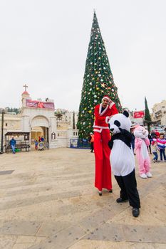 NAZARETH, ISRAEL - December 19, 2014: Santa Claus on stilts, other figures, local and visitors, and a Christmas tree, in the square of the Greek Orthodox Church of Annunciation, in Nazareth, Israel