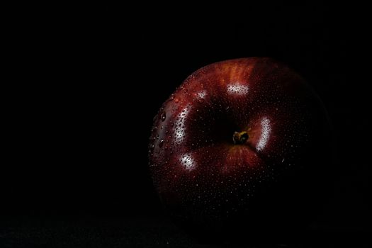 Close up fresh red Apple with water droplet isolated on black background – low key macro shoot