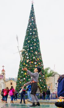 NAZARETH, ISRAEL - December 19, 2014: Jugglers, local and visitors, and a Christmas tree, in the square of the Greek Orthodox Church of Annunciation, in Nazareth, Israel