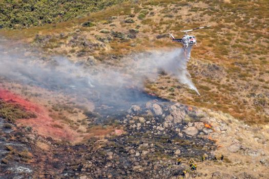 Winchester, CA USA - June 14, 2020: Cal Fire helicopter drops water on a dry hilltop wildfire near Winchester, California.