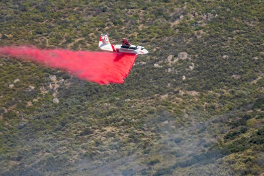 Winchester, CA USA - June 14, 2020: Cal Fire aircraft drops fire retardant on a dry hilltop wildfire near Winchester, California.