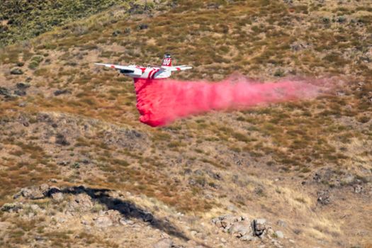 Winchester, CA USA - June 14, 2020: Cal Fire aircraft drops fire retardant on a dry hilltop wildfire near Winchester, California.