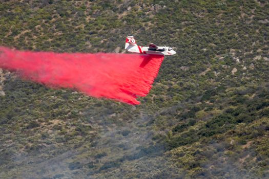 Winchester, CA USA - June 14, 2020: Cal Fire aircraft drops fire retardant on a dry hilltop wildfire near Winchester, California.