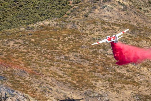 Winchester, CA USA - June 14, 2020: Cal Fire aircraft drops fire retardant on a dry hilltop wildfire near Winchester, California.