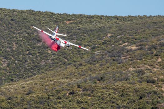 Winchester, CA USA - June 14, 2020: Cal Fire aircraft drops fire retardant on a dry hilltop wildfire near Winchester, California.