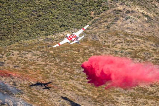 Winchester, CA USA - June 14, 2020: Cal Fire aircraft drops fire retardant on a dry hilltop wildfire near Winchester, California.