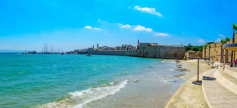 Acre, Israel - July 08, 2019: Panoramic view of the Horses beach, the sea wall and the fishing port, with locals and visitors, in the old city of Acre (Akko), Israel