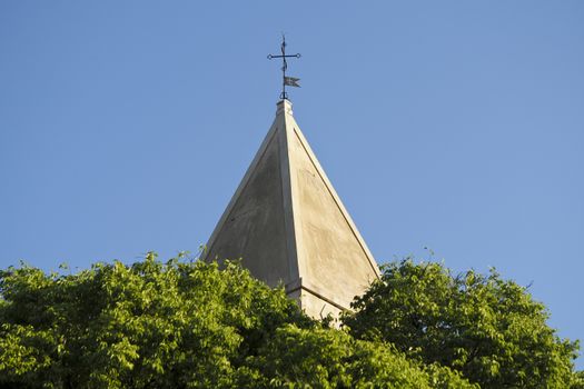 the top of the church tower above the tree, with the blue sky in the background