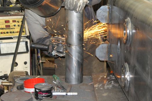 craftsman with working gloves cutting an iron bar with the electric angle grinder which sprays many hot sparks in the dark workshop, dangerous work, copy space