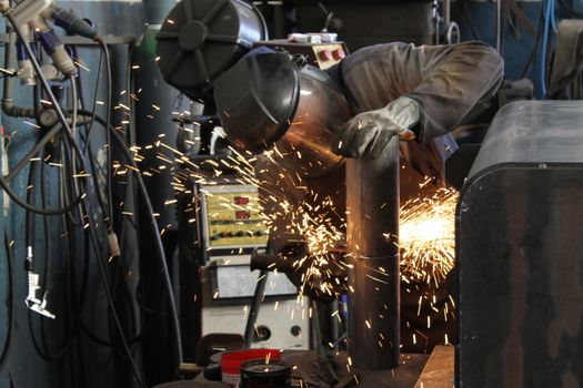 craftsman with working gloves cutting an iron bar with the electric angle grinder which sprays many hot sparks in the dark workshop, dangerous work, copy space