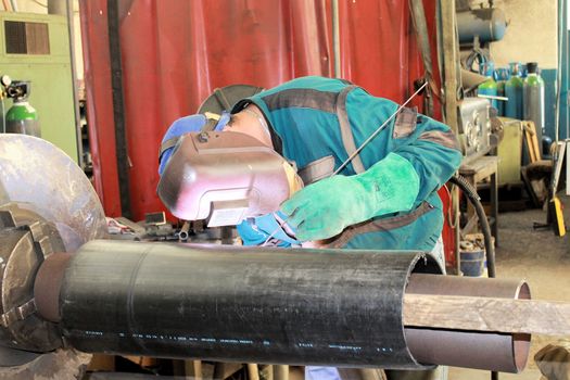 The welder is assembling valve to the pipe line with Tungsten Inert Gas Welding process (TIG). The welder wears protective equipment with a welding mask and heat resistant gloves.