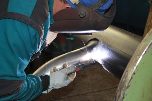 The welder is assembling valve to the pipe line with Tungsten Inert Gas Welding process (TIG). The welder wears protective equipment with a welding mask and heat resistant gloves.