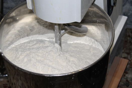 Mixing dough for bread baking with professional kneader spiral machine at the manufacturing. The dough is kneaded for burgers.