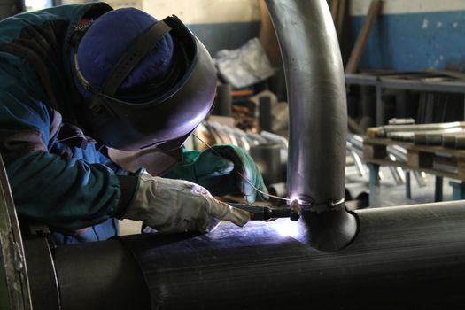 Welder Worker Performs Jump Welding. Worker Welder Performs Arc-Welding Process of Metal Structures. Flying Sparks From the Welding Machine. Welder Welds Metal Profiles for Second Floor Indoors