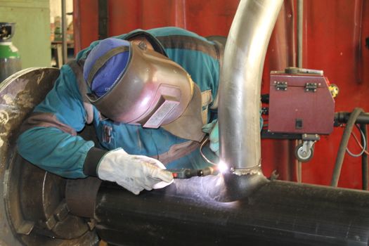 Welder Worker Performs Jump Welding. Worker Welder Performs Arc-Welding Process of Metal Structures. Flying Sparks From the Welding Machine. Welder Welds Metal Profiles for Second Floor Indoors