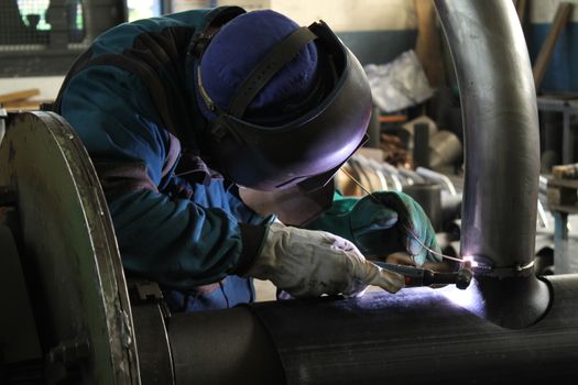 Welder Worker Performs Jump Welding. Worker Welder Performs Arc-Welding Process of Metal Structures. Flying Sparks From the Welding Machine. Welder Welds Metal Profiles for Second Floor Indoors