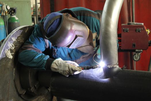 Welder Worker Performs Jump Welding. Worker Welder Performs Arc-Welding Process of Metal Structures. Flying Sparks From the Welding Machine. Welder Welds Metal Profiles for Second Floor Indoors