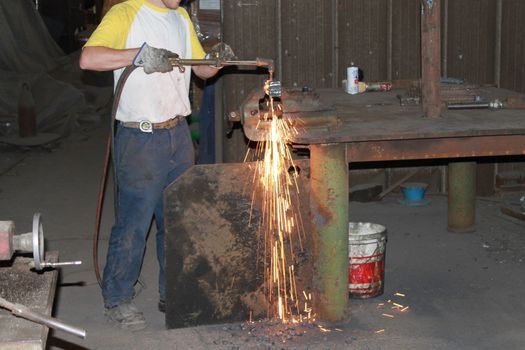 Worker is cutting manually old metal construction in container by using gas mixture of oxygen and acetylene, propane for repair work.