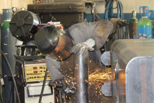 craftsman with working gloves cutting an iron bar with the electric angle grinder which sprays many hot sparks in the dark workshop, dangerous work, copy space