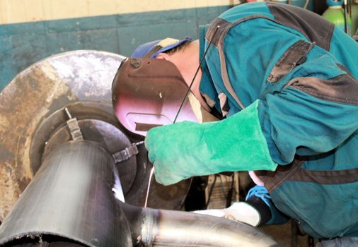 The welder is assembling valve to the pipe line with Tungsten Inert Gas Welding process (TIG). The welder wears protective equipment with a welding mask and heat resistant gloves.