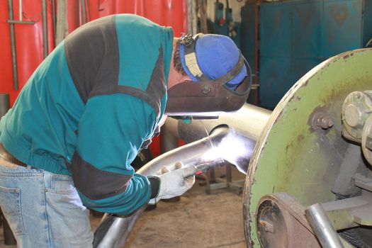 The welder is assembling valve to the pipe line with Tungsten Inert Gas Welding process (TIG). The welder wears protective equipment with a welding mask and heat resistant gloves.